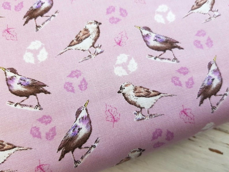 Op de afbeelding: Roze stof met een herhalend patroon van kleine vogels en gestileerde bladeren. De vogels zijn in tinten bruin, wit en paars.