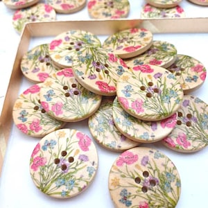 Könnte beinhalten: Ein Stapel Holzknöpfe mit Blumenmuster. Die Knöpfe sind cremefarben mit rosa, blauen und gelben Blumen. Die Knöpfe haben vier Löcher.