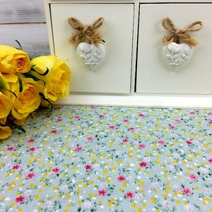 May include: A white wooden box with two drawers, each with a heart-shaped knob and a bow made of twine. The box is sitting on a light blue fabric with a floral pattern. A bouquet of yellow roses is in the foreground.