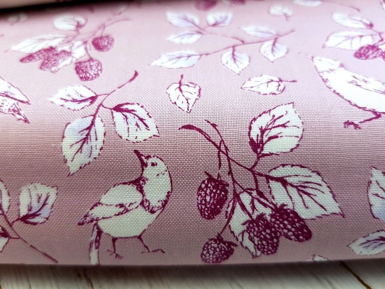 Op de afbeelding: Roze stof met een wit en bordeauxrood bloemenpatroon met vogels en bessen.