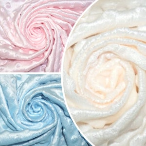 Op de afbeelding: Drie stofstalen in roze, wit en lichtblauw. Elke staal is een close-up van een textuurstof met een swirl-patroon.