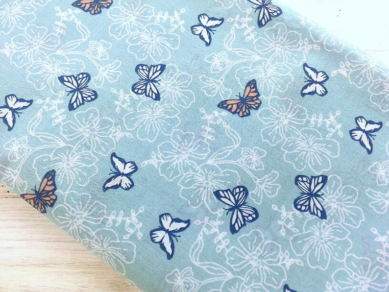May include: A light blue fabric with a white floral pattern and a repeating design of orange and blue butterflies.