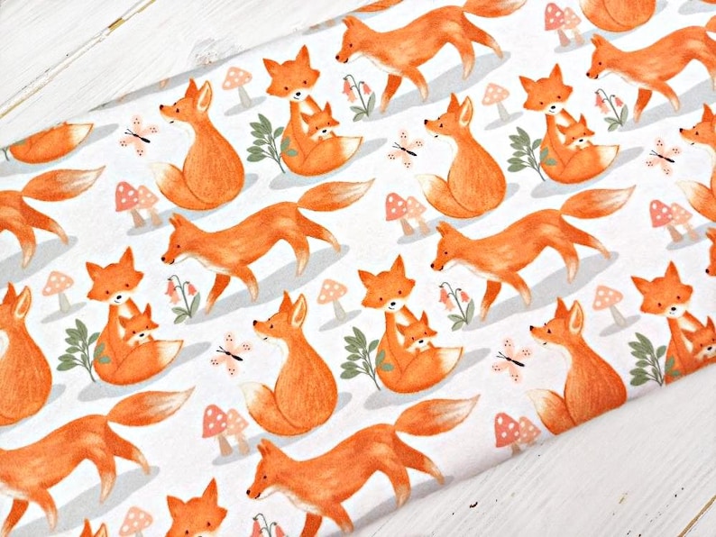 May include: White fabric with a repeating pattern of orange foxes. The foxes are depicted in a cartoon style, with some holding a smaller fox cub. The background is white with small pink and white mushrooms and butterflies.