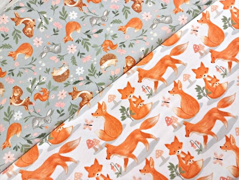 May include: Two fabric swatches with different patterns. The top swatch is light gray with a repeating pattern of foxes, squirrels, deer, rabbits, and flowers. The bottom swatch is white with a repeating pattern of orange foxes with their cubs.