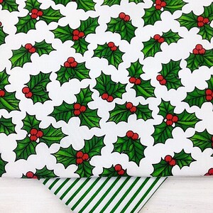 May include: White fabric with a repeating pattern of green holly leaves with red berries. A green and white striped fabric is folded on top of the holly fabric.