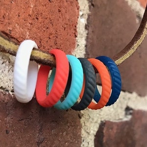 May include: A set of seven silicone rings in various colors, including white, orange, turquoise, black, and blue. The rings are stacked on a brown leather strap.