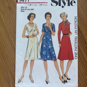 May include: A vintage sewing pattern for a dress, featuring three different styles. The pattern is labeled "Style" and "1471". The dress styles include a white dress with a scoop neck, a blue floral dress with a scoop neck, and a red dress with a Peter Pan collar. The pattern is for size 16, bust 97 cm (38 inches).