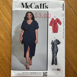 Op de afbeelding: McCall's naaipatroon M8340 met een vrouw in een marineblauwe jurk met een V-hals en een split aan de voorkant. Het patroon bevat illustraties van twee andere jurk ontwerpen. De tekst op het patroon luidt "McCall's" en "Designed and printed in USA."