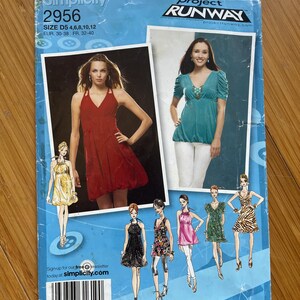 May include: Simplicity sewing pattern number 2956 for a dress, sizes D5 4, 6, 8, 10, 12, EUR 30-38, FR 32-40. The pattern is inspired by Project Runway and features a variety of styles, including a red sleeveless dress, a turquoise top with a beaded neckline, and a yellow dress with a ruffled neckline.