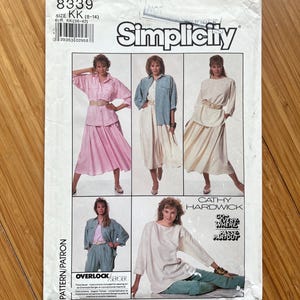 Könnte beinhalten: Simplicity Schnittmuster Nummer 8339 für die Größen KK (8-14) und EUR KK (36-42). Das Schnittmuster bietet vier verschiedene Stile von Oberteilen und Röcken, darunter ein weißes Oberteil mit Rundhalsausschnitt, ein hellblaues Oberteil mit Knopfleiste, ein rosa Oberteil mit Knopfleiste und ein weißer Rock mit gerafftem Bund.