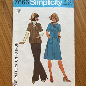 Puede incluir: Patrón de costura vintage Simplicity número 7666 para un vestido y una blusa. El patrón es para talla pequeña, 8-10. El patrón muestra a dos mujeres usando las prendas. Una mujer lleva un vestido azul con un cuello blanco y un cinturón blanco. La otra mujer lleva una blusa marrón con un cuello blanco y pantalones marrones.