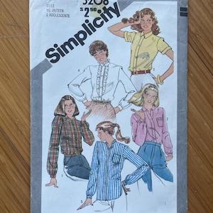 May include: A vintage Simplicity sewing pattern for blouses, with the number 5208 and a price of £2.50. The pattern is for sizes 11/12, and includes the text "YG. JR/TEEN" and "J. ADOLESCENTE". The cover features illustrations of different blouse styles.