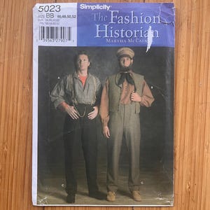 May include: A Simplicity sewing pattern envelope, number 5023, titled The Fashion Historian by Martha McCain. The cover displays two outfits: one with a striped shirt, braces, and dark trousers, and another with a waistcoat, patterned shirt, and trousers.