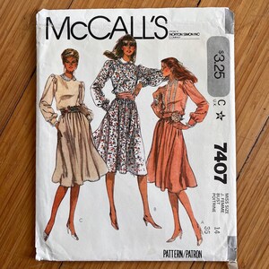 May include: A McCall's sewing pattern envelope 7407 for a dress in size 14, featuring illustrations of three variations of the garment with long sleeves, gathered waists, and mid-calf skirts. The cover displays the text McCall's, 7407, and 36 bust.