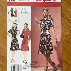 May include: Simplicity sewing pattern number 1587, size US 14-22, for a 1940s retro dress. The pattern shows a black and white floral dress with a white collar and short sleeves. The pattern also includes a red dress with a white collar and short sleeves. The pattern is for a dress with a fitted bodice and a full skirt.