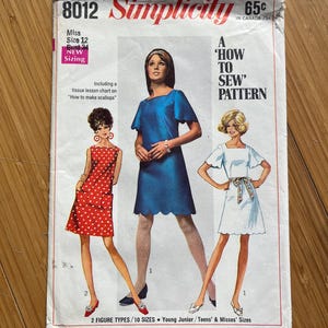 May include: A vintage Simplicity sewing pattern, number 8012, for a dress. The pattern is for sizes 12 and 34 bust. The pattern includes instructions on how to make scallops. The pattern is titled "A 'How To Sew' Pattern".