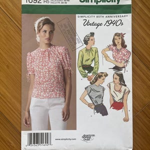 May include: Simplicity sewing pattern with a vintage 1940s theme. The pattern shows a woman in a floral top and white trousers. Illustrations of various blouse styles are also included. The pattern size is U.S. 6,8,10,12,14, equivalent to Euro sizes 32-40.