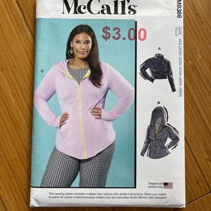 Op de afbeelding: Een McCall's naaipatroon met een vrouw in een lichtpaarse hoodie met rits. Het patroon bevat illustraties van jasontwerpen en de tekst "$3.00". Het patroon is ontworpen en gedrukt in de VS.