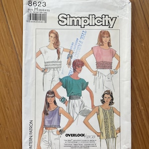 Könnte beinhalten: Simplicity Schnittmuster Nummer 8623 für die Größen 6, 8 und 10. Das Schnittmuster enthält Anleitungen zum Nähen eines bauchfreien Oberteils mit verschiedenen Rüschendetails. Das Schnittmuster ist für die Verwendung mit einer Overlock- oder Coverstich-Nähmaschine gedacht.