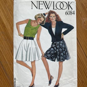 May include: Vintage New Look sewing pattern number 6084. The pattern features two women wearing different styles of shorts. One woman is wearing a white pair of shorts with a black belt and a green tank top. The other woman is wearing a black and white floral print pair of shorts with a black blazer.