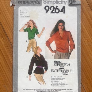 Peut inclure: Une pochette de patron de couture Simplicity 9264 pour un haut à col châle. Le recto présente des illustrations de trois variantes du haut en vert, orange et noir, associées à des pantalons. Le texte inclut Pattern/Patron, 9264 et Time Saver Stretch.
