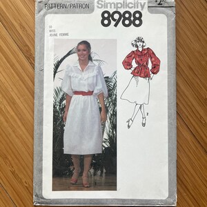 Peut inclure: Un patron de couture Simplicity vintage, numéro 8988, avec une photo d'une femme portant une robe blanche avec une ceinture rouge. Le patron comprend également un dessin d'une blouse rouge et d'une jupe blanche. Le texte "MISS JEUNE FEMME" est visible.