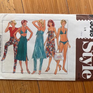 Peut inclure: Une enveloppe de patron de couture rectangulaire en papier étiquetée Style 3048. Le devant présente des illustrations de cinq tenues, dont un haut rouge avec un pantalon à fleurs, un ensemble jupe bleu sarcelle, une robe bustier bleue et un bikini.