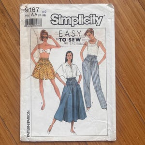 Peut inclure: Une pochette de patron de couture Simplicity 9167, taille AA, illustrant trois tenues : une jupe à motif floral, une jupe midi bleue unie et un pantalon rayé. Le texte indique Easy To Sew, Simplicity et Pattern/Patron.