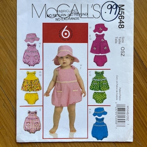 May include: A sewing pattern for a baby girl's dress and matching hat. The pattern is for size OSZ and includes instructions for making a pink gingham dress, a yellow floral dress, a green polka dot dress, and a blue gingham dress. The pattern is from McCall's and is number M5648.