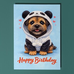 May include: A greeting card featuring a cute puppy wearing a panda hoodie. The puppy has brown and black fur and is smiling. The card has a light blue background with red hearts and the words "Happy Birthday" in red script.