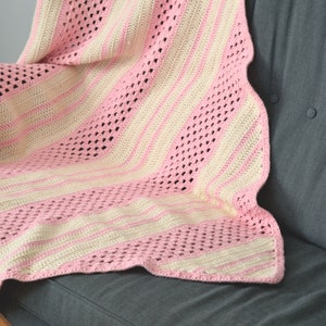 May include: A handmade crochet blanket featuring alternating vertical stripes of soft pink and cream yarn. The design incorporates sections of solid double crochet stitches alongside rows of open, airy mesh patterns. The text mycrochetory.com is visible.