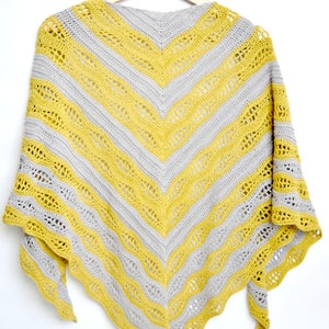 May include: A handmade, chevron-patterned shawl in yellow and gray. The shawl is made of yarn and is hanging on a wooden hanger against a white background. The design features alternating stripes of yellow and gray, with a lacy, openwork pattern.