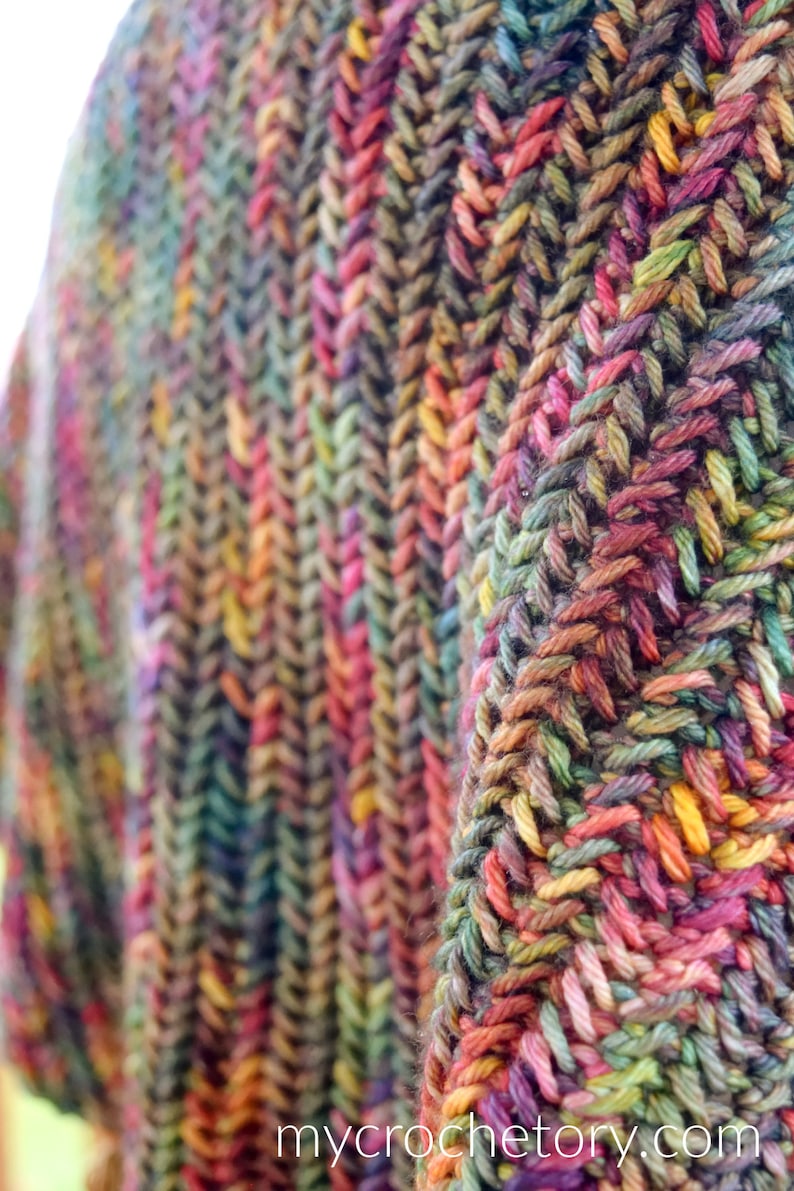 Puede incluir: Primer plano de una tela de crochet multicolor con un patr&oacute;n de punto de espiga. La tela est&aacute; hecha con una variedad de tonos de hilo marr&oacute;n, verde, rojo, naranja y amarillo.