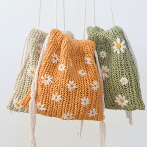 May include: Three crocheted bags with daisy flower embroidery. The bags are in shades of green, orange, and beige. Each bag has a white drawstring.