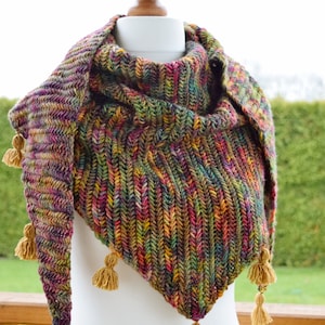 Puede incluir: Un chal triangular de lana multicolor con tonos de verde, marr&oacute;n, morado y rojo. El chal tiene un patr&oacute;n de punto texturizado y est&aacute; terminado con borlas doradas.