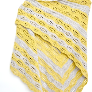 May include: A yellow and gray crocheted shawl with a striped pattern. The shawl is hanging on a wooden hanger against a white background. The design features alternating bands of yellow and gray, with a scalloped edge.