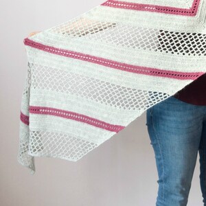 Puede incluir: Un chal triangular de ganchillo con secciones alternas de puntos sólidos gris claro y malla abierta, acentuado por rayas horizontales en hilo magenta oscuro. En la esquina inferior izquierda aparece un logotipo circular con el texto My Crochetory.