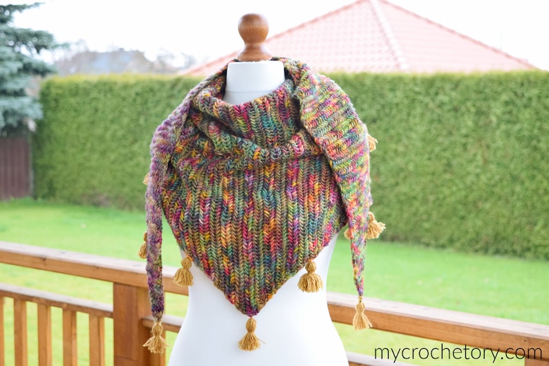 Puede incluir: Un chal de ganchillo colorido con forma triangular y borlas. El chal est&aacute; hecho con una variedad de colores, incluyendo verde, azul, rojo y amarillo.