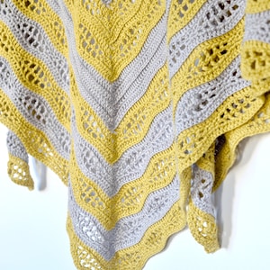 May include: A handmade crochet shawl in a chevron pattern. Alternating bands of gray and yellow yarn create a striking visual effect. The shawl's edges are finished with a scalloped border, adding a touch of elegance to the design.