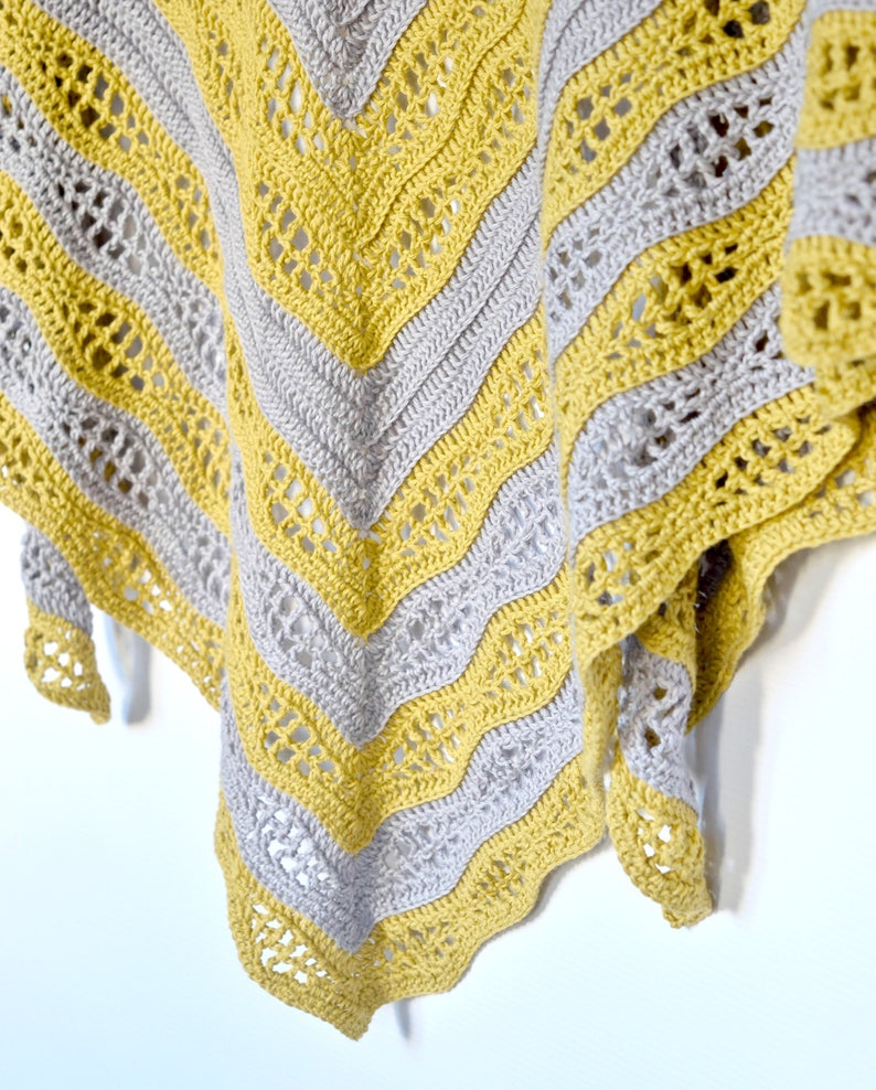 May include: A handmade crochet shawl in a chevron pattern. Alternating bands of gray and yellow yarn create a striking visual effect. The shawl's edges are finished with a scalloped border, adding a touch of elegance to the design.