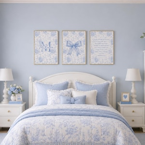 May include: A bedroom with a white bed, blue bedding, and matching pillows. Three framed prints with floral patterns and blue accents hang above the bed. Two white bedside tables with lamps flank the bed. A white bookshelf is on the right.