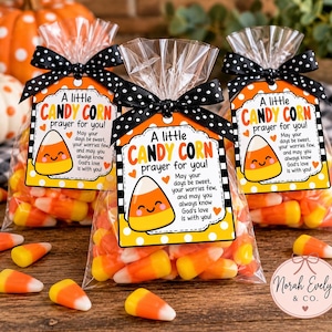 May include: Three clear plastic bags filled with yellow, orange, and white candy corn. Each bag is tied with a black and white polka dot ribbon and features a tag that reads A little CANDY CORN prayer for you! with a smiling candy corn graphic.