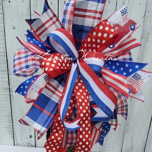 May include: A red, white and blue patriotic bow with a red, white and blue plaid ribbon, a white ribbon with red polka dots, and a red, white and blue ribbon with stars and a red truck graphic. The bow is attached to a black lantern.