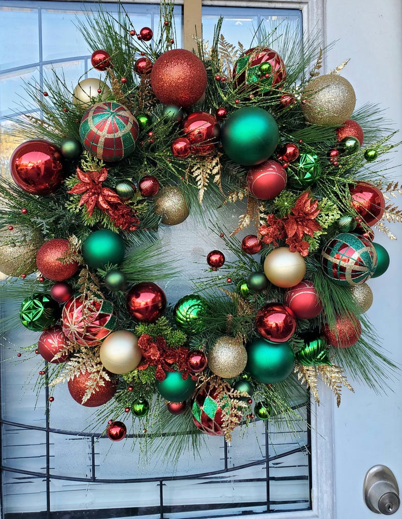May include: A Christmas wreath decorated with red, green, and gold ornaments. The wreath is made of pine branches and has a variety of different ornaments, including balls, stars, and bows.