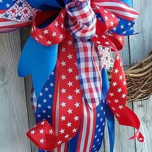 May include: A red, white, and blue patriotic bow with stars and stripes, gingham, and solid blue ribbon. The bow is tied around a wreath.