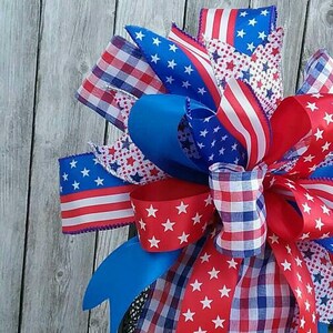 May include: A red, white, and blue patriotic bow with stars and stripes, checkered, and solid blue ribbon, tied around a black lantern.