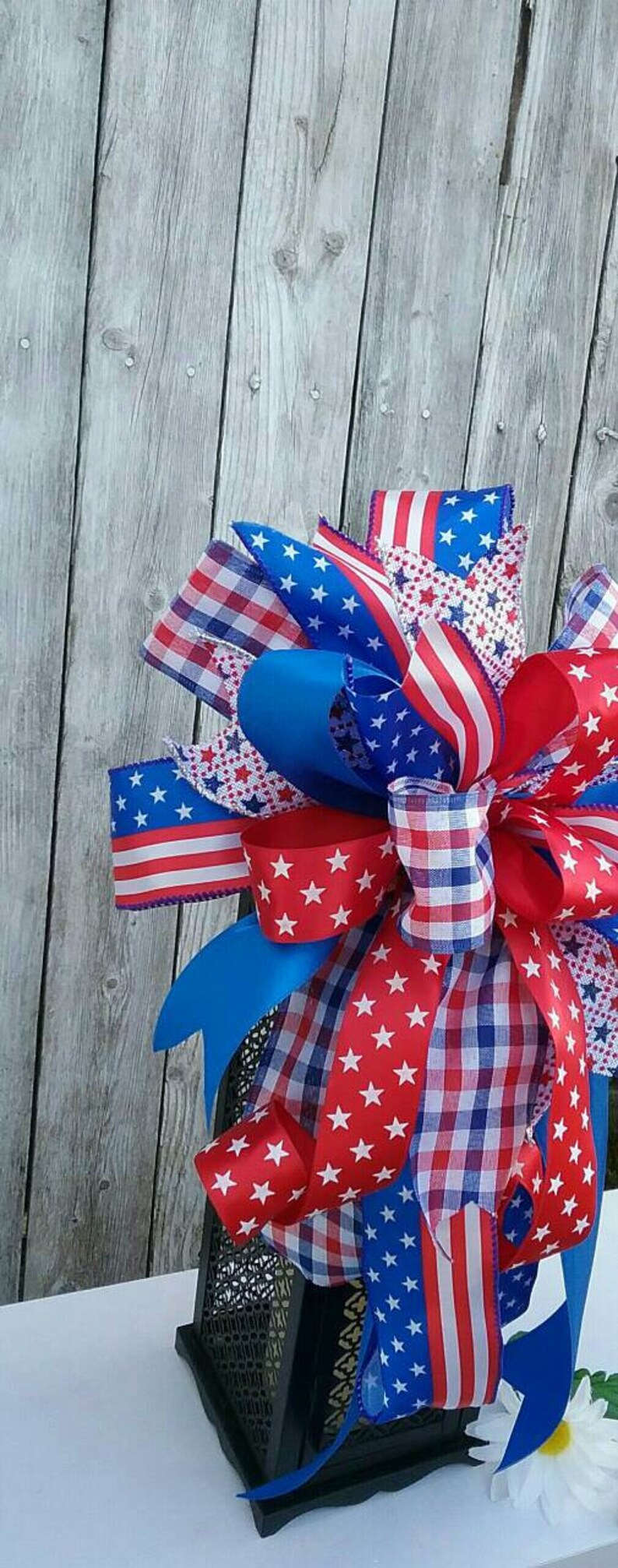 May include: A red, white, and blue patriotic bow with stars and stripes, checkered, and solid blue ribbon, tied around a black lantern.