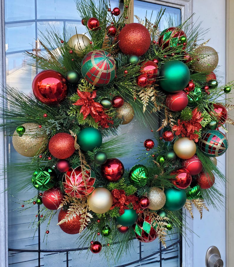 May include: A Christmas wreath decorated with red, green, and gold ornaments. The wreath is made of pine branches and has a variety of different ornaments, including round ornaments, star ornaments, and ribbon ornaments.