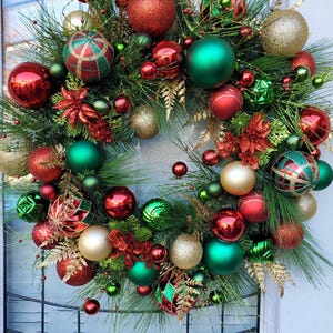 May include: A Christmas wreath decorated with red, green, and gold ornaments. The wreath is made of pine branches and has a variety of different ornaments, including balls, stars, and bows.