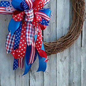 May include: A red, white, and blue ribbon wreath with a grapevine base. The ribbon is patterned with stars and checks.
